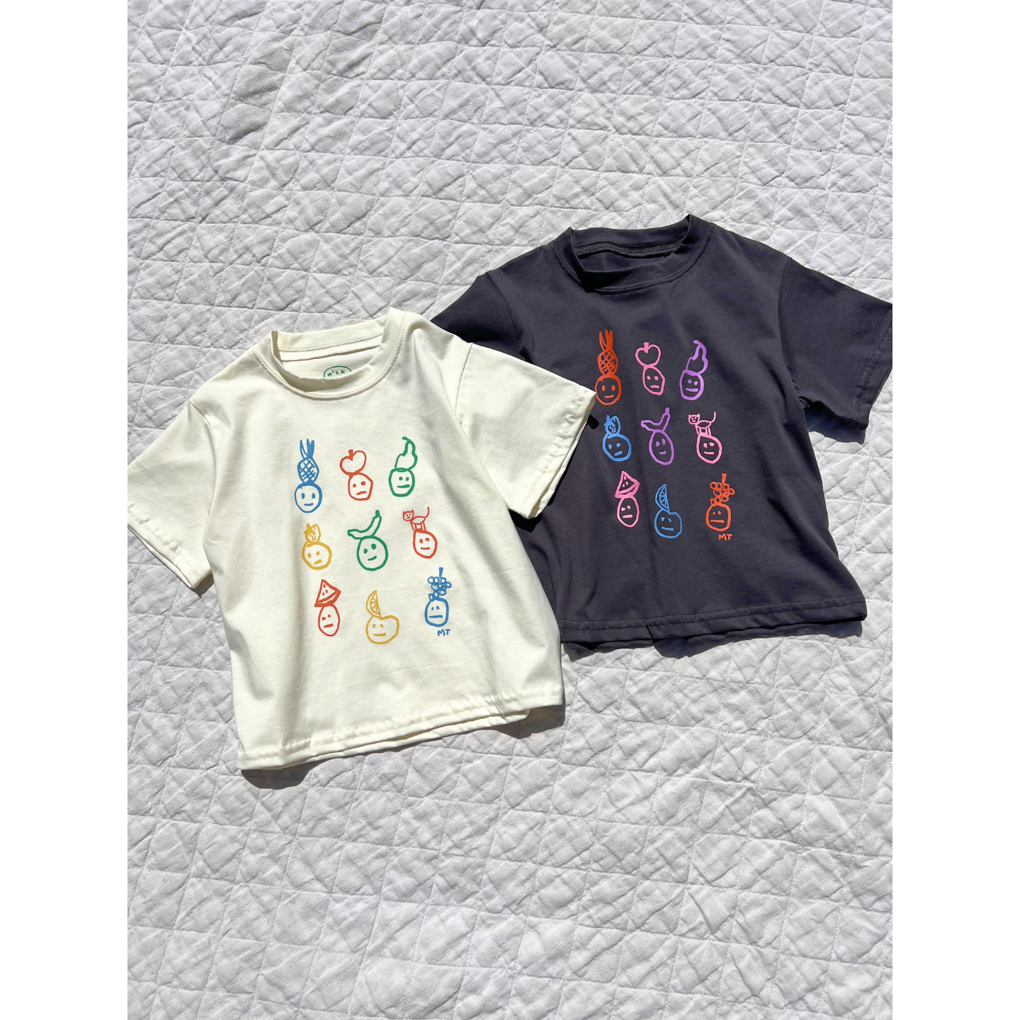 Charcoal | Cream and charcoal color ways of fruit dace tees laid flat on the blanket