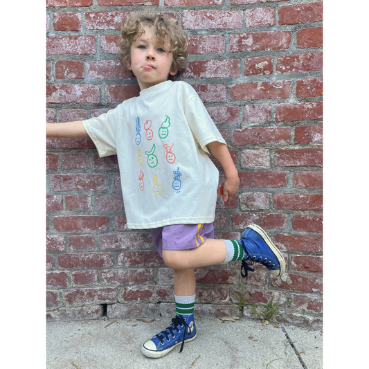 Ivory | A child Is wearing an ivory colorway of the fruit face tee with purple shorts.