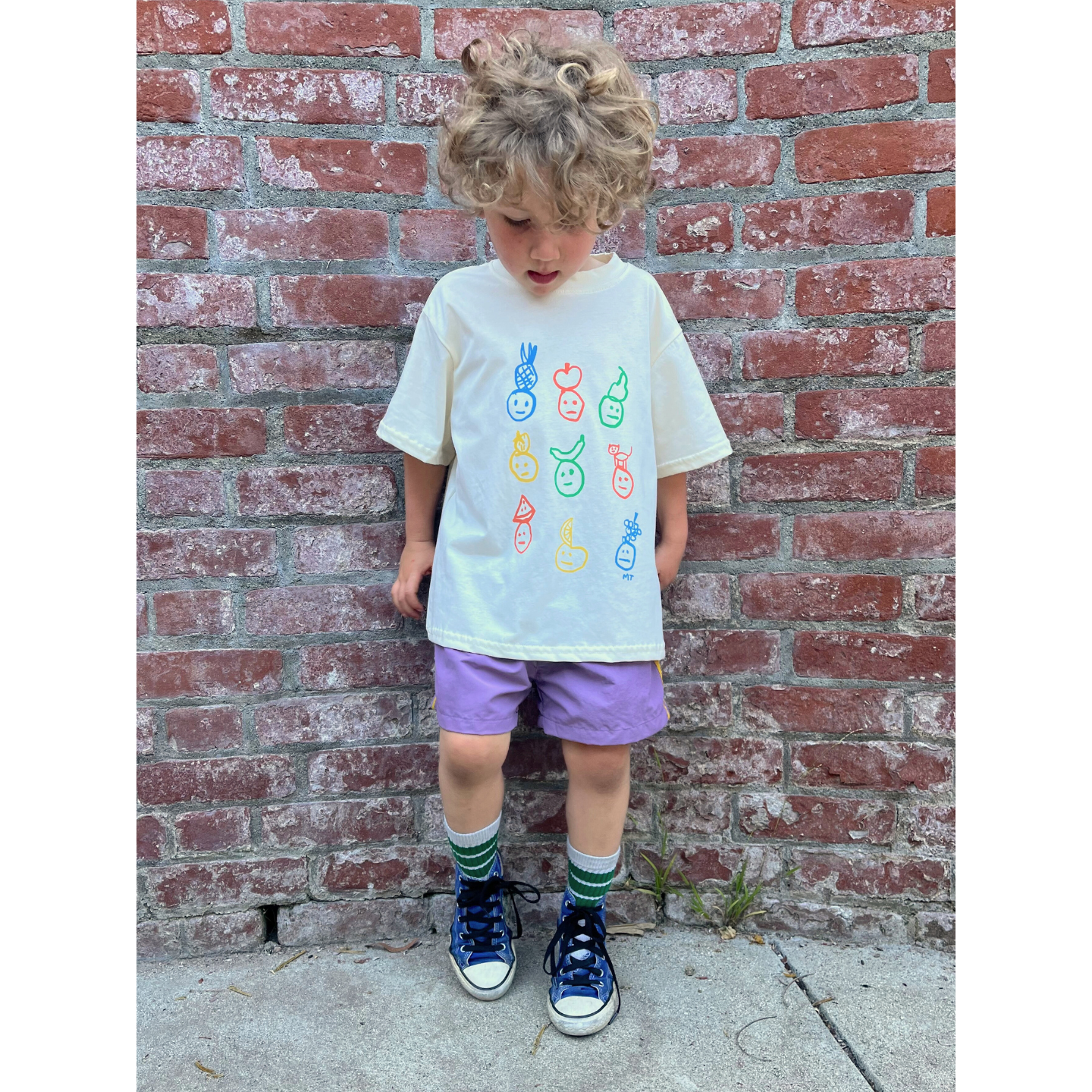 Ivory | A child Is wearing an ivory colorway of the fruit face tee with purple shorts.