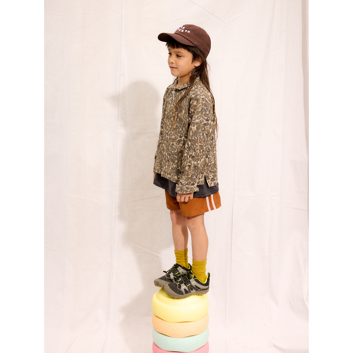Rust | A child is wearing the rust Sprinter Shorts with a leopard jacket and Milk Teeth Hat