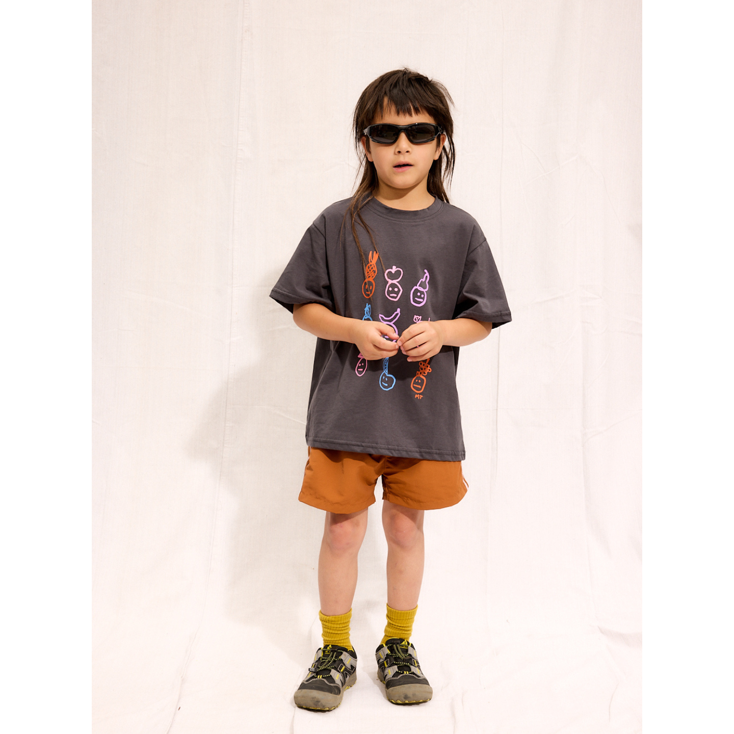 Charcoal | A child is wearing a charcoal Fruit Face tee with rust Sprinter Shorts and sneakers.