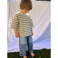 Medium Wash | A child wearing the Double Trouble baggy jeans in medium-blue denim with two large patch pockets of lighter denim. He wears an oversized striped t-shirt in cream, with black stripes, and stands in front of a white sheet, standing on grass.