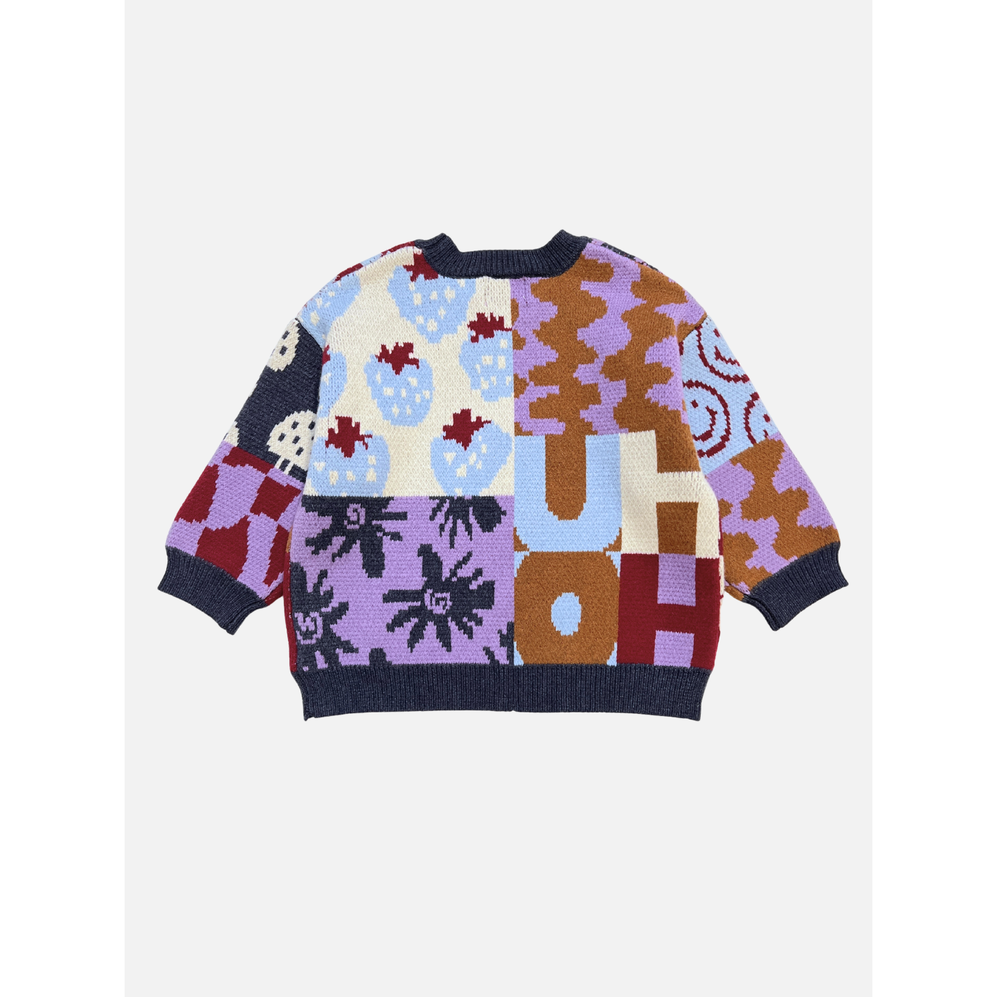 The EVERYTHING SWEATER is a colorful, oversized soft knit with bold letters and patterns like strawberries, wavy checkers, and abstract shapes on a white background.