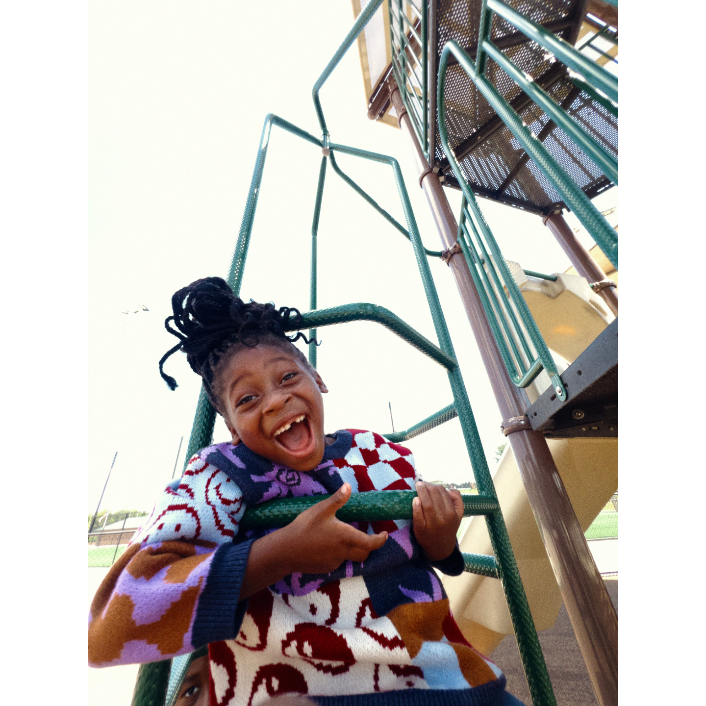 Child playing on a playground structure with a colorful sweater