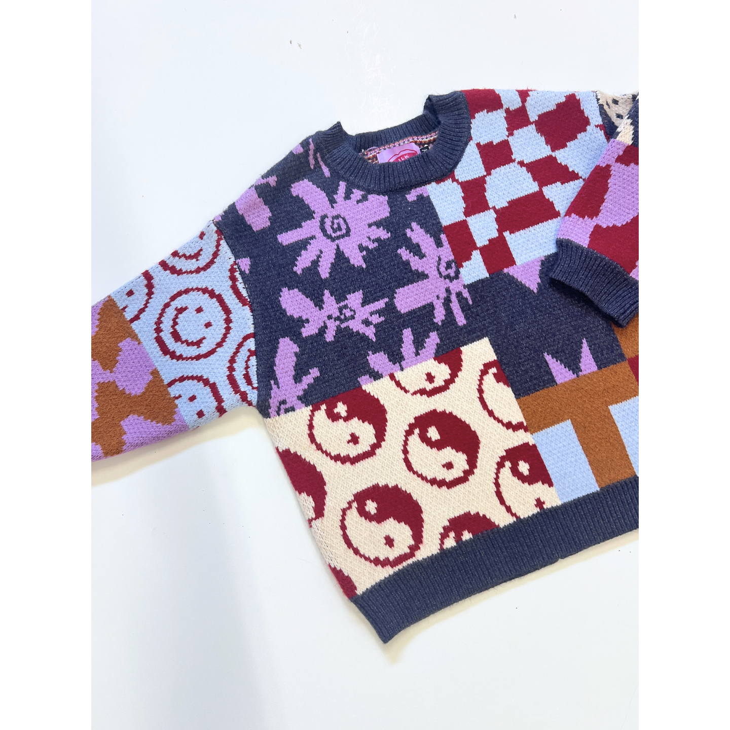 The EVERYTHING SWEATER is a soft knit featuring geometric wavy checkers, smiley faces, animal prints, and yin-yang patterns in red, blue, cream, purple, and brown.